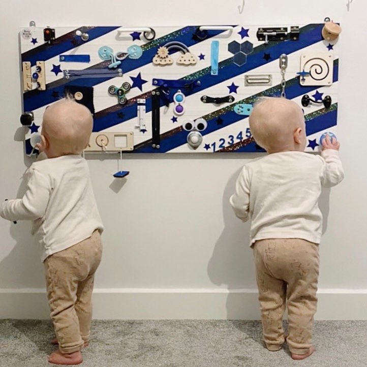 Twins playing on a wall mounted Busy Board